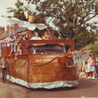 Float dressed as the 'Jolly Roger' with 'Peter Pan' written on a sail. Crowds watching below a grassy bank | Nuneaton Memories