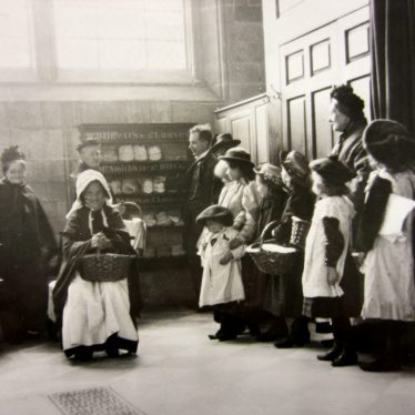 Woman in bonnet collecting loaf in a basket, children in pinafores and others waiting; loaf rack on the inside wall of the church | Warwickshire County Record Office reference PH1035/B3351