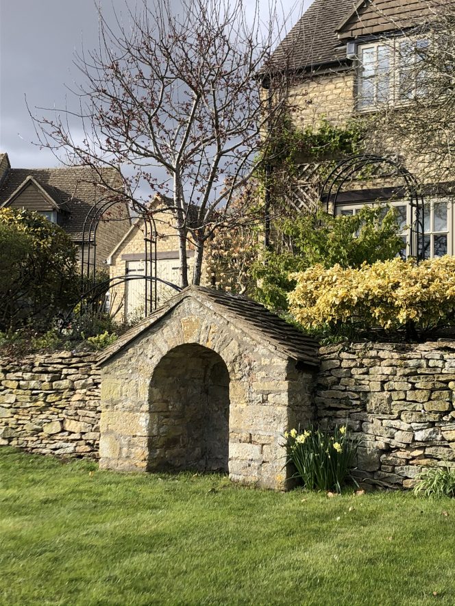 Stone water fountain in centre of photo with stone wall to either side and stone houses in background | Anna Rossiter
