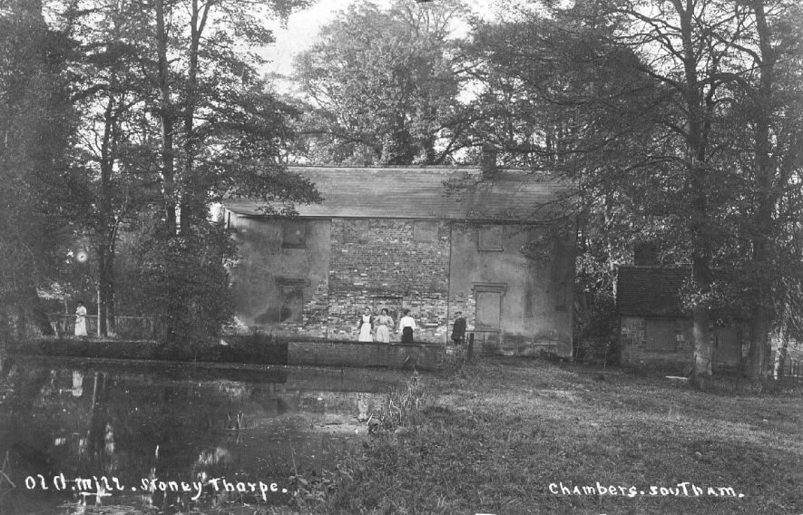Old Mill, Stoneythorpe; view of mill across the millpond, five people standing outside. Photo: Chambers, Southam (no.939).  c.1905 |  IMAGE LOCATION: (Warwickshire County Record Office)
