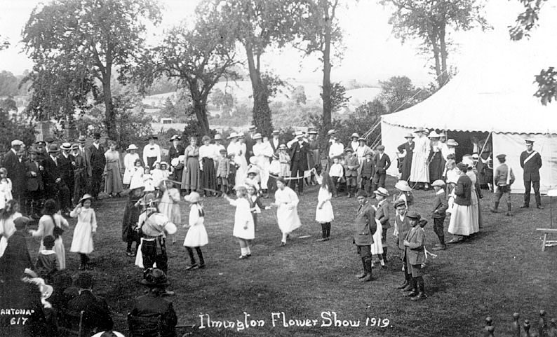 Children dancing during Flower Show, Ilmington.  1919.

[The musician playing the fiddle, with his back to the camera and standing at the head of the line of girls performing the ribbon dance is Sam Bennett(1865-1951) |  IMAGE LOCATION: (Warwickshire County Record Office)