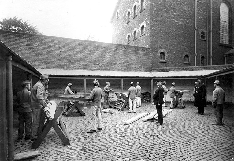 Prisoners in Warwick prison sawing wood and being watched over by two prison officers.  c.1906 |  IMAGE LOCATION: (Warwickshire County Record Office) IMAGE DATE: (c.1906)