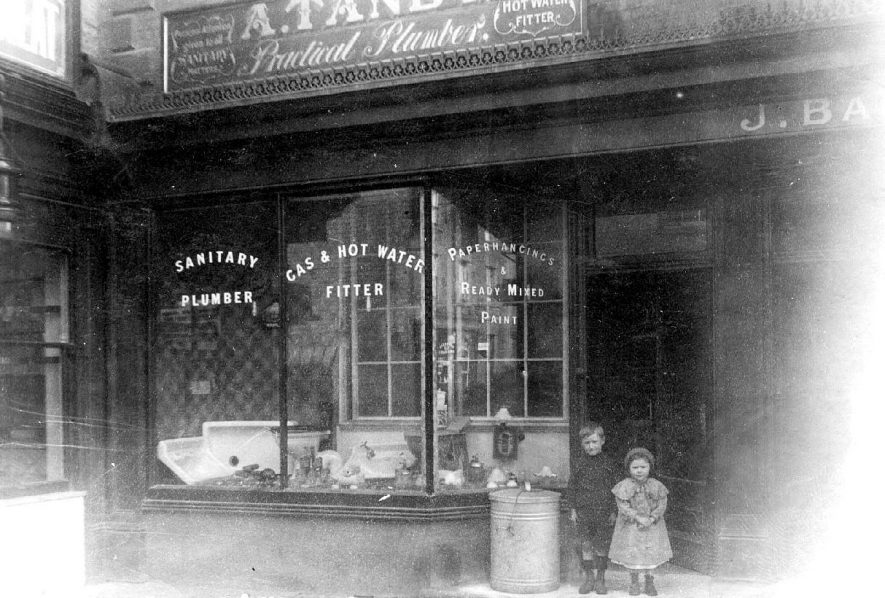 Tandy's shop in Swan Street, Warwick, with sign for sanitary, plumbers, gas, painting and wall hanging supplies. Two children standing at the entrance. 1920s |  IMAGE LOCATION: (Warwickshire County Record Office)