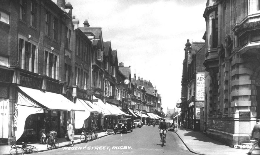 Regent Street, Rugby, showing shops with living accommodation above, clock and advertising on shops, bicycles and motor cars.  1930s |  IMAGE LOCATION: (Warwickshire County Record Office)