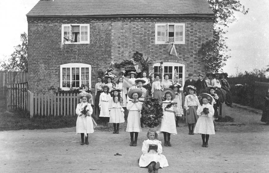 Group of children and adults outside a cottage dressed for May Day, two girls carrying a garland, Long Itchington.  1911 |  IMAGE LOCATION: (Warwickshire County Record Office)