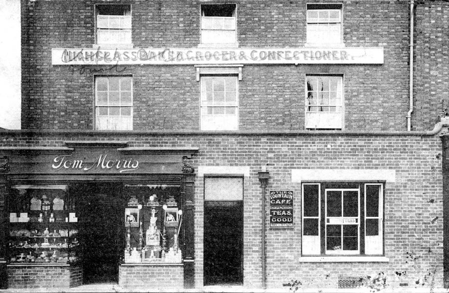 Exterior of Tom Morris's bakers shop and the Fountain Cafe, Henley Street, Stratford upon Avon.  1910s
[It is thought that this photograph was actually taken from the American Fountain in Rother Street. Windsor Street is just to the left of Tom Morris's shop] |  IMAGE LOCATION: (Warwickshire County Record Office)