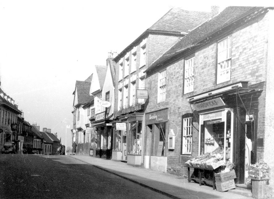 High Street, Coleshill, above Church Hill up to church lych gate, showing Hardwick's greengrocers, Sketchley's cleaners, Turner's hardware and Taylor's bakers.  1970 |  IMAGE LOCATION: (Coleshill Library)