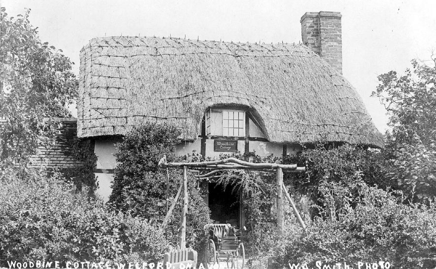 A thatched and half timbered house known as Woodbine cottage, Welford on Avon. Note the old perambulator at the entrance.  1910s |  IMAGE LOCATION: (Warwickshire County Record Office)