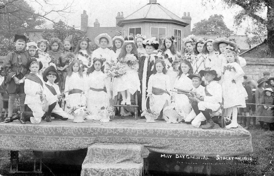 The May Queen and her courtiers on a platform with a summer house and the speak pipe in the background.  1910s |  IMAGE LOCATION: (Warwickshire County Record Office)