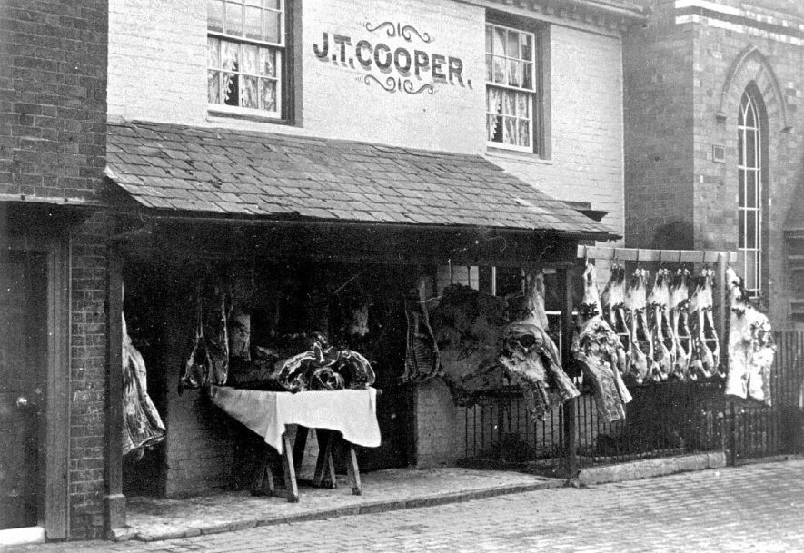 J T Cooper butcher's shop showing carcasses hanging outside and chapel to left, Alcester.  1910 |  IMAGE LOCATION: (Warwickshire County Record Office)