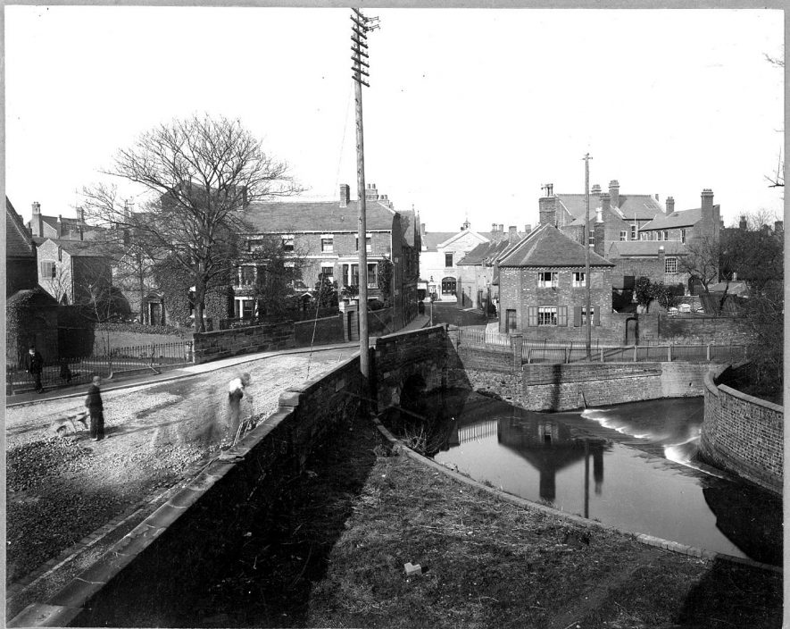Mill Walk, Nuneaton. River in the foreground, with small bridge over and houses in the background. Part of this is now the site of the Council house.  1900s |  IMAGE LOCATION: (Nuneaton Library)