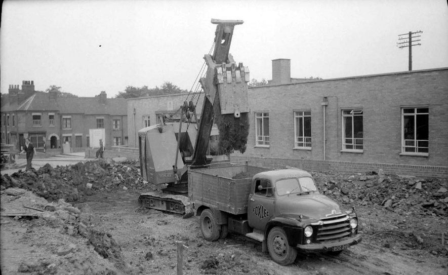 Excavator at work on the construction of a new road from Leicester Road to Church Street, Nuneaton. Offices of inland Revenue in the background.  June 13th 1959 |  IMAGE LOCATION: (Warwickshire County Record Office)