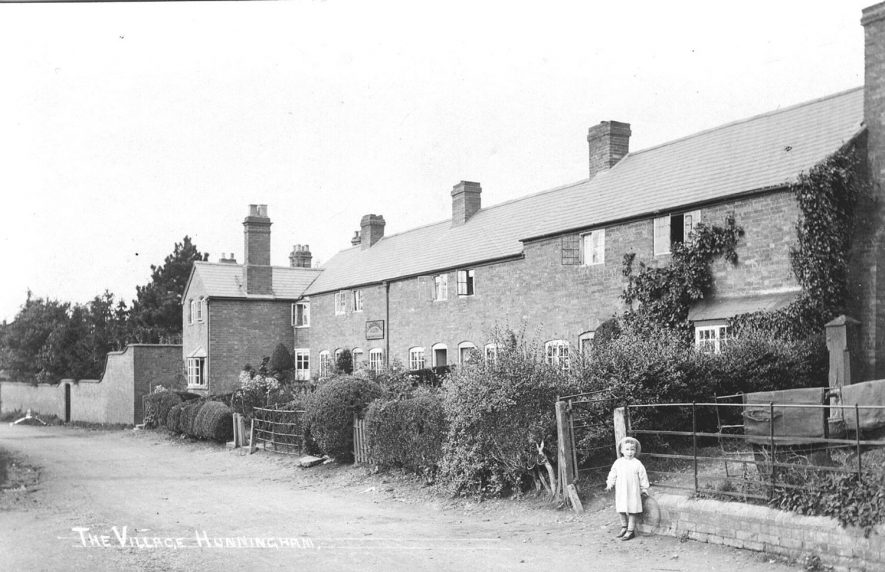 Elm Farm Cottages in Hunningham with a little girl standing in front of a water pump.  The cottage at the end of the row is Vine Cottage.  1920s |  IMAGE LOCATION: (Warwickshire Museums. Photographic Collections.)