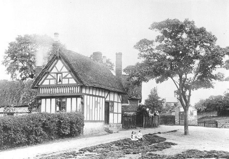 A thatched and timber framed house in Whitnash with two children sitting in front.  1900s |  IMAGE LOCATION: (Warwickshire Museums. Photographic Collections.)