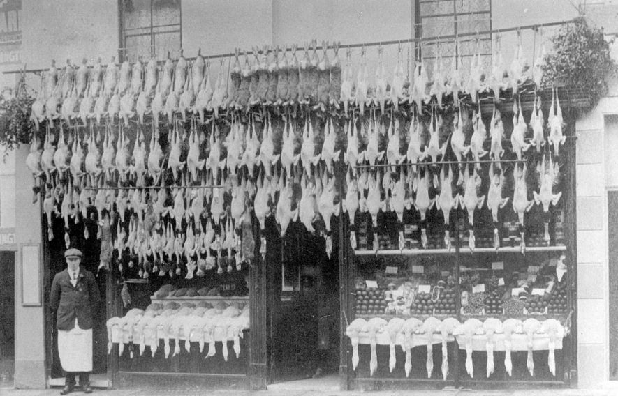 Shop of William Metcalf, game & poultry dealer, showing Christmas display, and the proprietor can be seen outside the shop, Clemens Street, Leamington Spa.  1910s |  IMAGE LOCATION: (Leamington Library) PEOPLE IN PHOTO: Metcalf, William