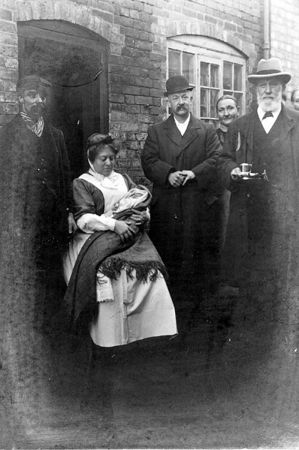 A mine worker with his wife and child outside his cottage with William Johnson M.P. holding a tea-cup.  1900 |  IMAGE LOCATION: (Warwickshire County Record Office) PEOPLE IN PHOTO: Johnson, W MP, Johnson as a surname