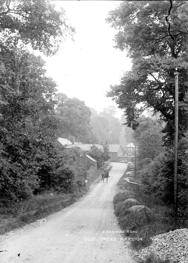 Horse being led along Hardwick Road, Priors Marston, with village houses in the background.  1920s |  IMAGE LOCATION: (Warwickshire County Record Office)