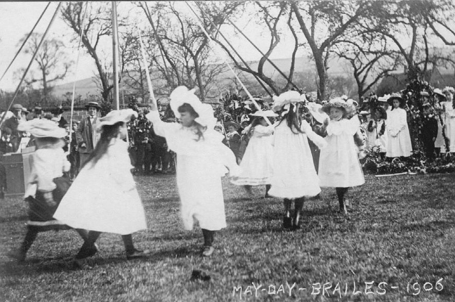 Lower Brailes May-Day celebrations in meadow, with girls in fancy hats dancing  round the may pole, on-lookers and harmonium.  1906 |  IMAGE LOCATION: (Warwickshire County Record Office)