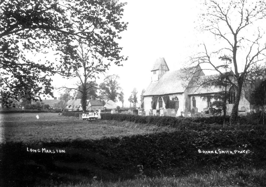 St James church and churchyard, Long Marston. A group of girls are sitting on a seat in the field in front of the church.  1900s |  IMAGE LOCATION: (Warwickshire County Record Office)
