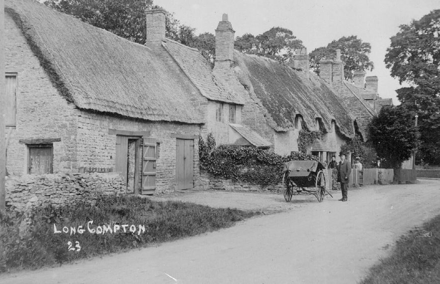 Village street in Long Compton showing thatched cottages and barns. Man standing beside pony trap and two women in garden.  1910s |  IMAGE LOCATION: (Warwickshire County Record Office)