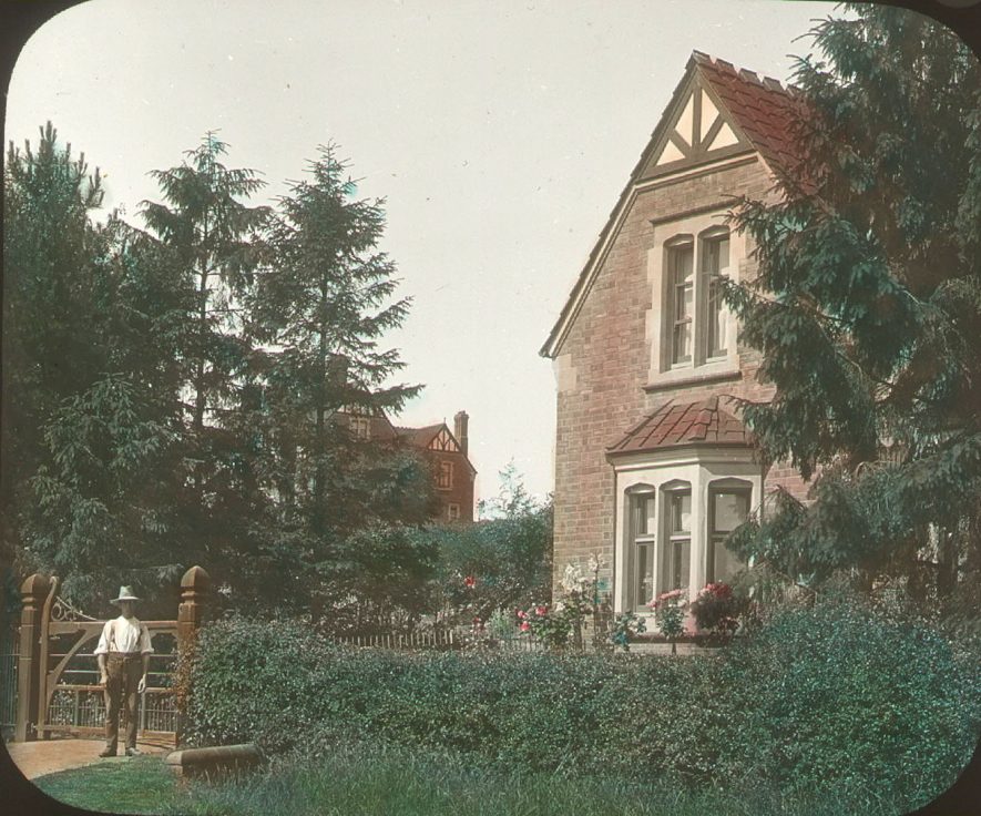 Red Hill House, garden and coach house, Clifford Chambers. A man is standing in front of the gate.  1900s |  IMAGE LOCATION: (Warwickshire County Record Office)