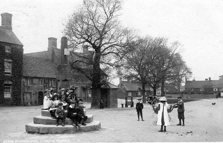 The square, with broken Cross and stocks, Dunchurch. Children sitting on steps of Cross with garlands.  1900s |  IMAGE LOCATION: (Warwickshire County Record Office)