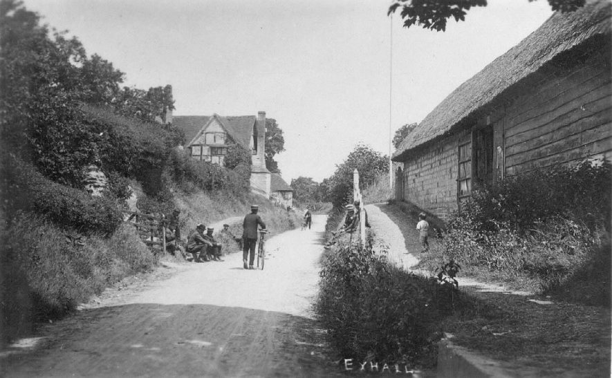 Road with timbered house and barn. Labourers seated at roadside, Exhall. Two men with bicycles.  1910s |  IMAGE LOCATION: (Warwickshire County Record Office)