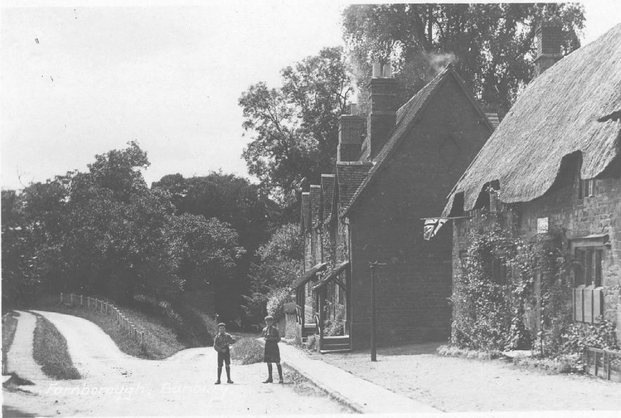 Part of street at end of village with stone cottages, one thatched, Farnborough. Two boys in street. Union Jack at cottage window.  1920s |  IMAGE LOCATION: (Warwickshire County Record Office)