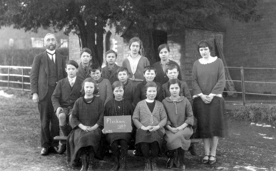 Group photograph of teachers and pupils, Flecknoe. Board reading 
