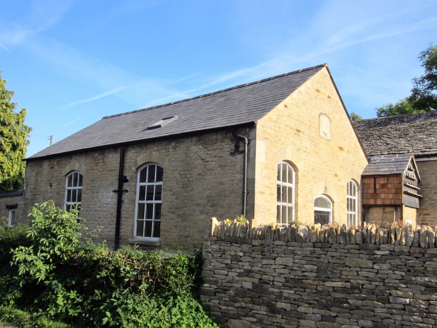 1-storey, stone-built, slate roof (with skylight), large arched windows, plaque on end; modern dovecote beside and dry stone wall in front | Image courtesy of Anne Langley