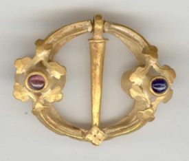 A medieval brooch found near Warwick. Two coloured stones are either side of the golden circle, uneven in form, which has a straight piece of metal bisecting the circle. | Image courtesy of Warwickshire Museum