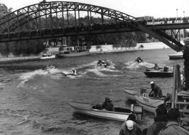 Action from the Six Heures de Paris speedboat race. The wash comes from behind the speedboats, that are all in a line as the spectators look on. | Warwickshire County Record Office reference CR4804