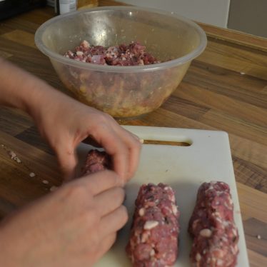 Moulding the mix into rough sausage shapes. The mixture is in the background, and in the foreground are large tube-like segments of sausagemeat. | Photograph by Ruth Long