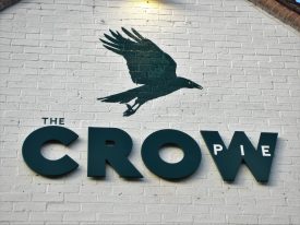 Crow Pie pub sign, Bilton, 2018. Flying black crow painted on white brick wall with title 'The CROW pie' on | Image courtesy of Anne Langley