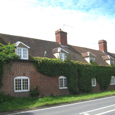 Former Coughton almshouses (front), 2018. A brick terrace with bushes covering much of the brickwork. | Image courtesy of Anne Langley
