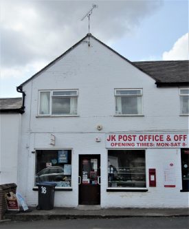 White-painted 2-storey brick building with modern windows and red letters on sign 'JK Post Office & Off [Licence] Opening times: Mon-Sat 8-?' | Image courtesy of Anne Langley