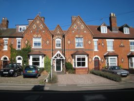 2-3-storey red-brick terrace with patterns in contrasting brick, white-painted bay windows and door arches, tiled roof and cars parked in front gardens | Image courtesy of Anne Langley