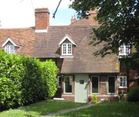 Back of former Coughton almshouse. Red brick and timber frame building with more modern porch added below and tiled roof with dormer window and large brick chimney above. Lawn, laurel hedge, garden path and trees | Image courtesy of Anne Langley